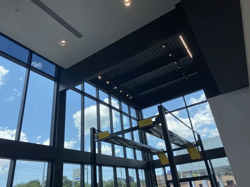 Double-height storefront interior with a black-painted ceiling deck and linear lighting above a glass curtain wall