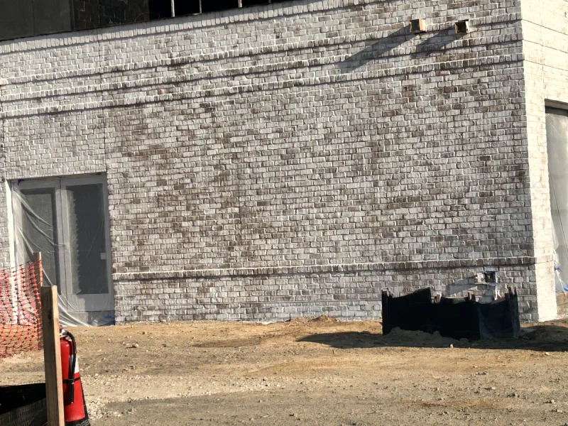 Large brick wall part-way through a lime-white coating, the original red brick still showing through
