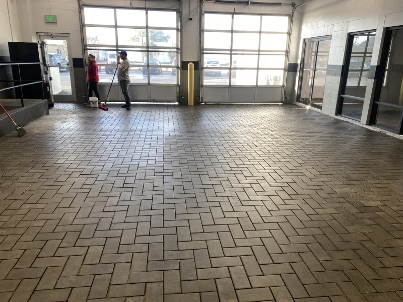 Crew washing a herringbone paver floor inside a service bay with the roll-up doors open