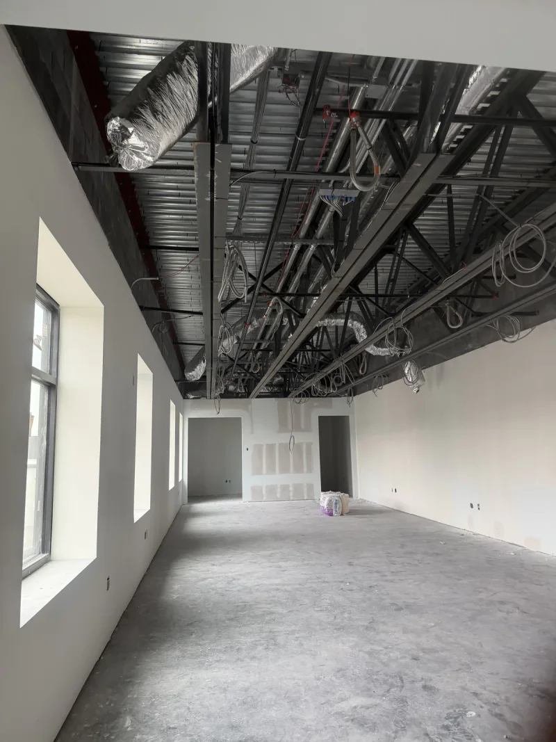 Finished drywall and painted white walls below an exposed black ceiling deck and ductwork