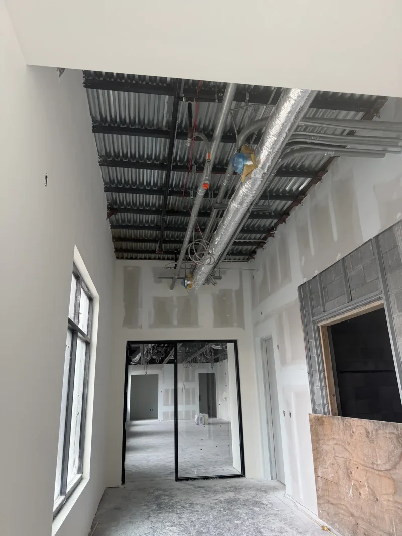 Drywall finishing under an open ceiling, with spiral ductwork and steel joists left exposed