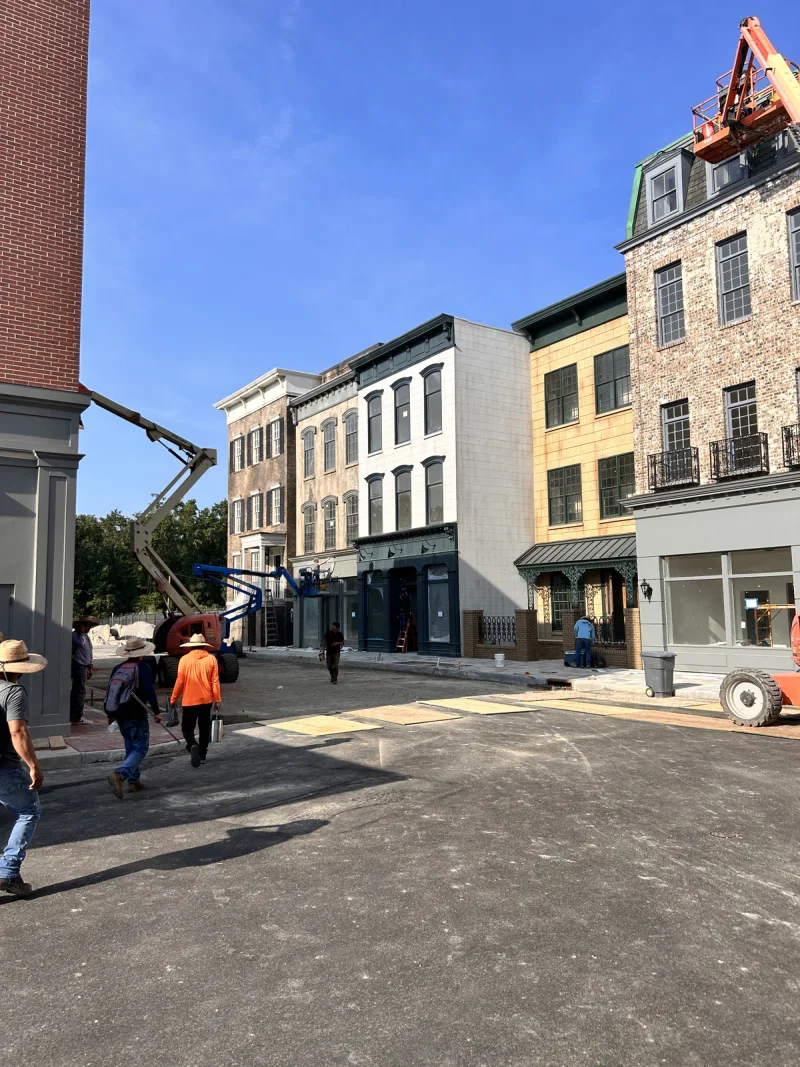 Crew crossing the street between painted storefronts, with a boom lift set up at the far corner