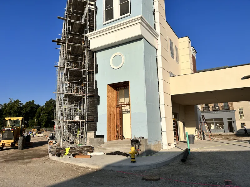 Scaffolding standing against a pale blue tower elevation with an oculus window and timber doors