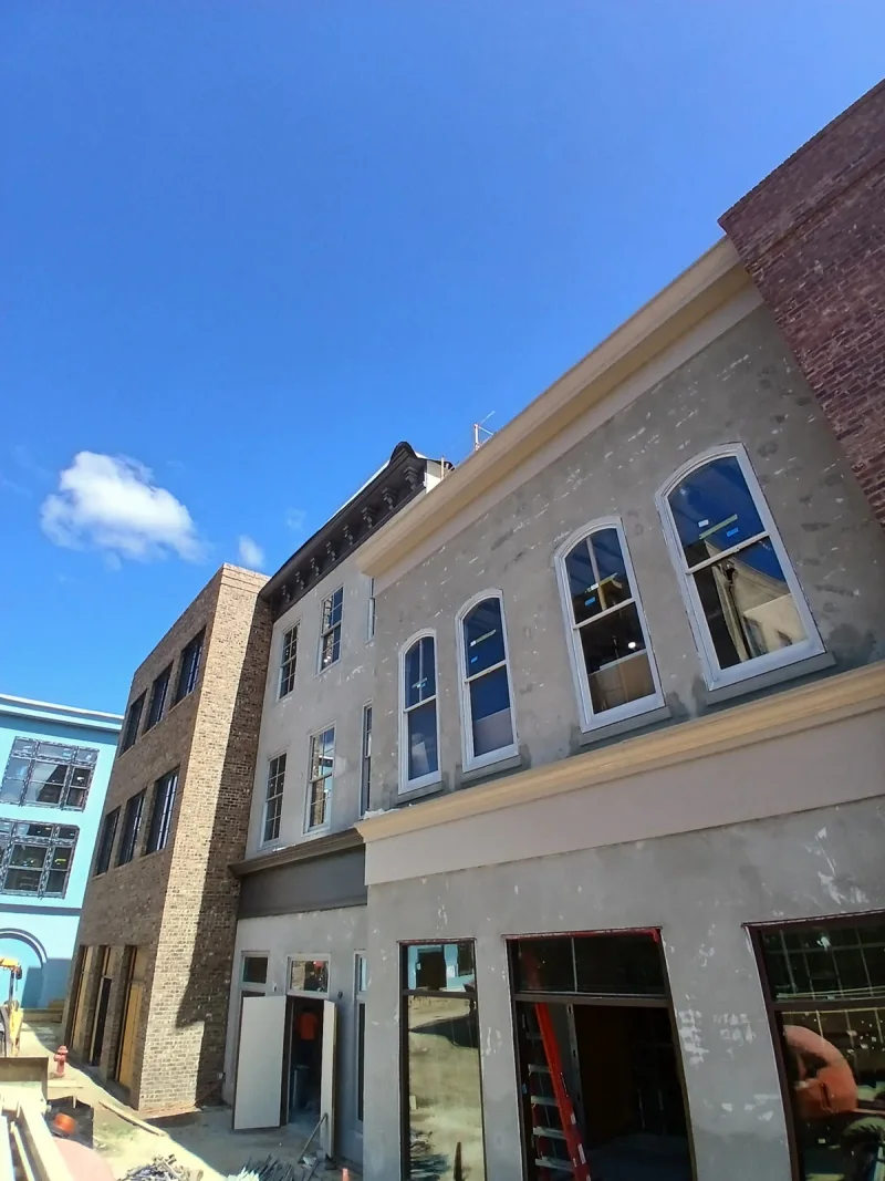 Street elevation of a stucco and brick block, arched windows and painted trim part-way through finishing