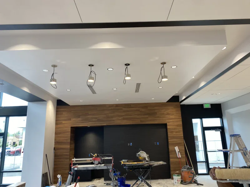 Wood-slat feature wall and black panel below a white stepped ceiling during interior fit-out