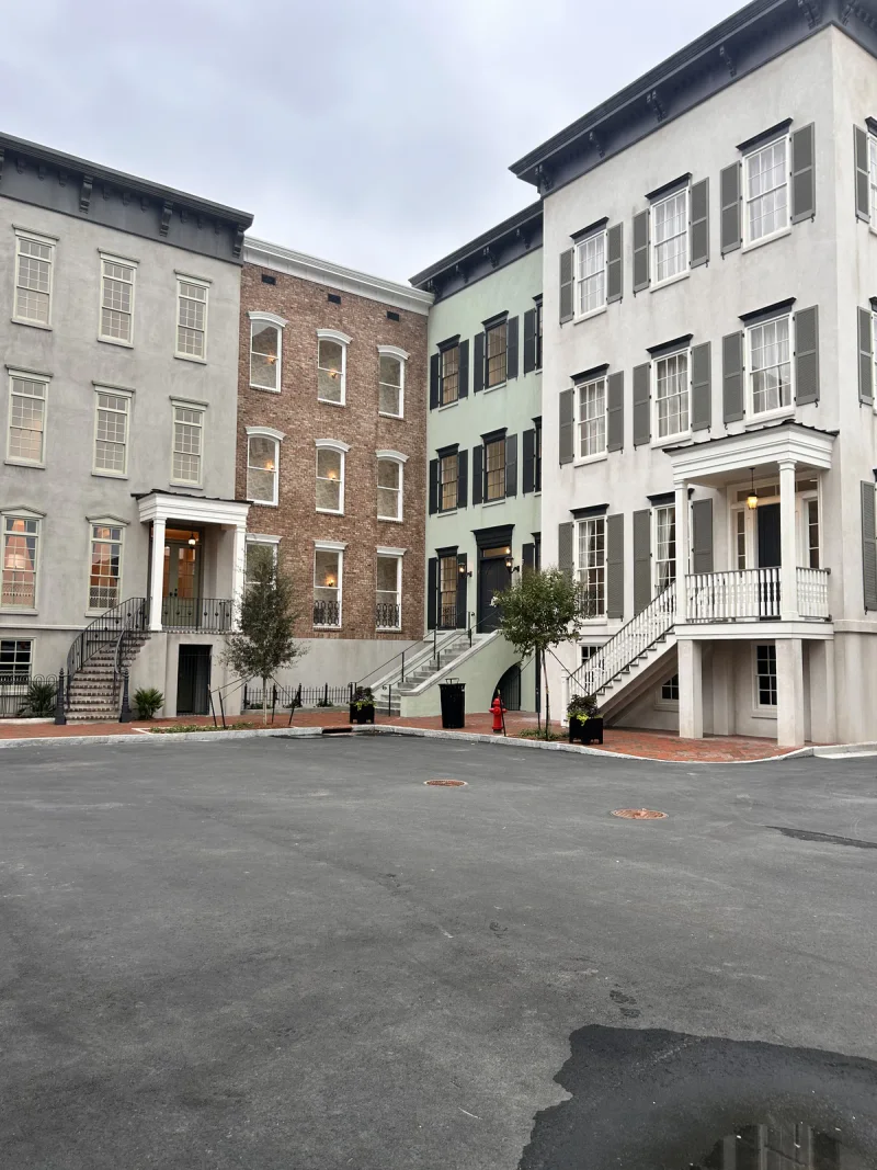 Finished row of townhouse facades in grey, green and exposed brick with painted stoops and railings