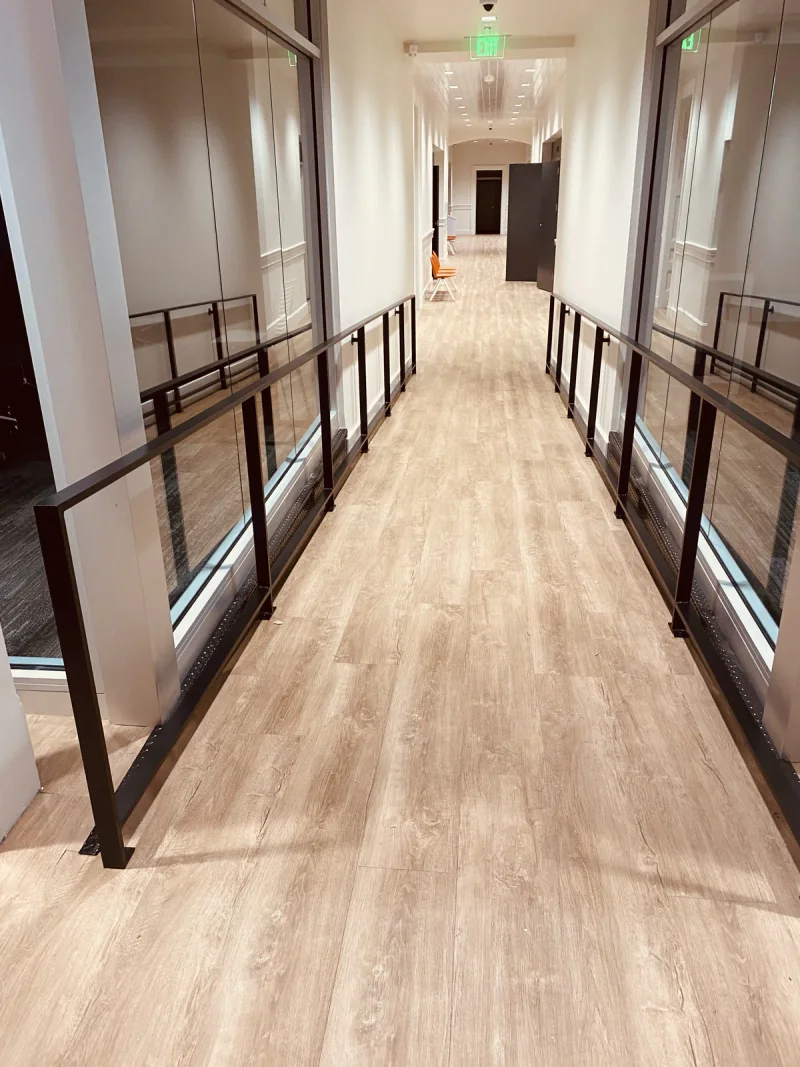 Interior walkway lined with black metal railings above new plank flooring