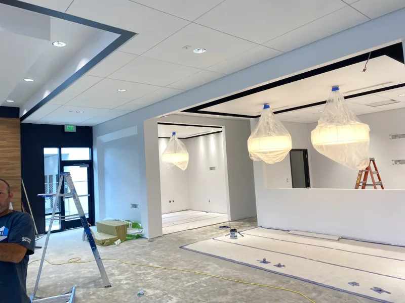 Open office area painted white with recessed ceiling coves and pendant lights still bagged