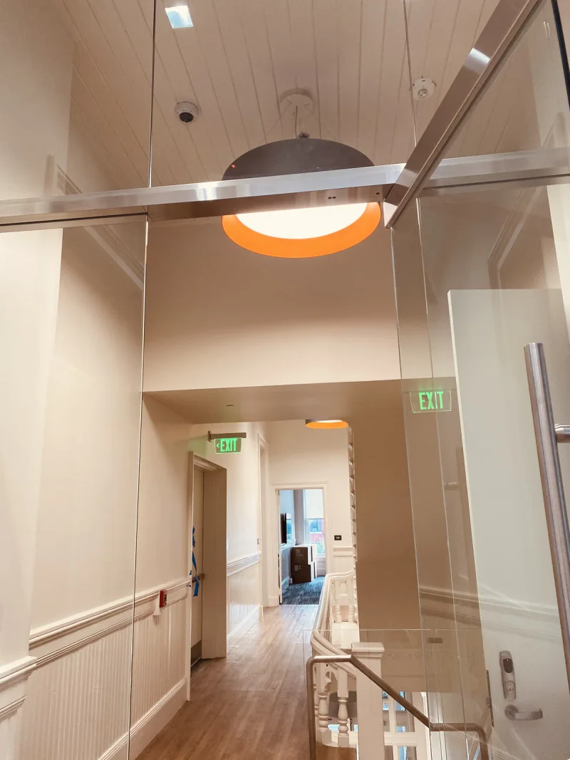 Double-height landing with a glass balustrade and a warm pendant above painted walls