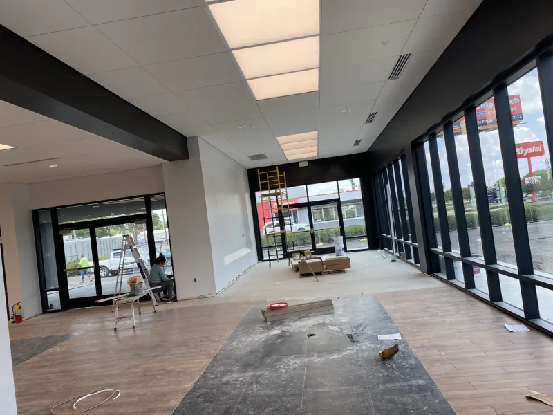 Retail floor with black-painted structural beams and full-height glazing while flooring goes in