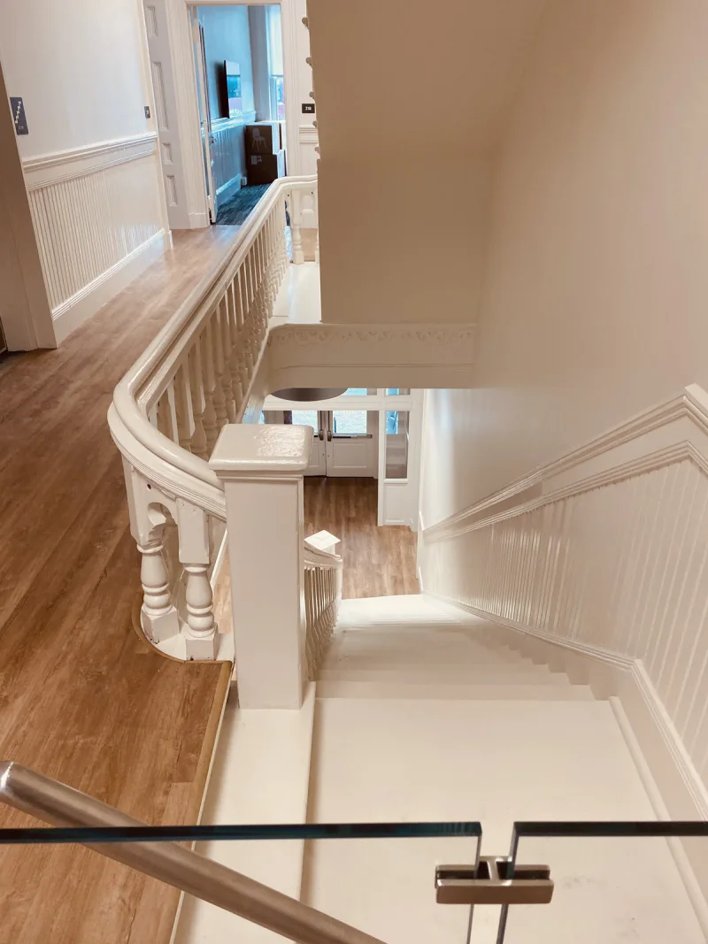 Curved staircase with turned white balusters and painted wainscot seen from the landing above