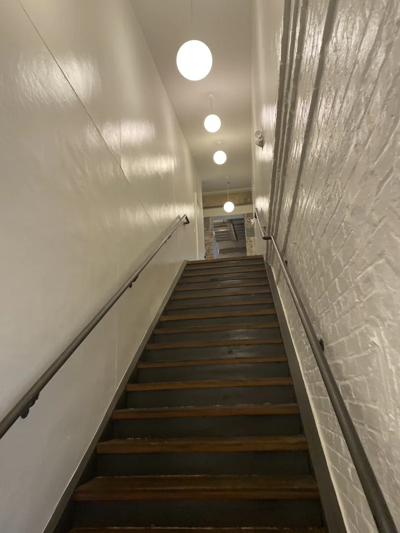 Narrow stairwell painted white with globe pendants above timber treads