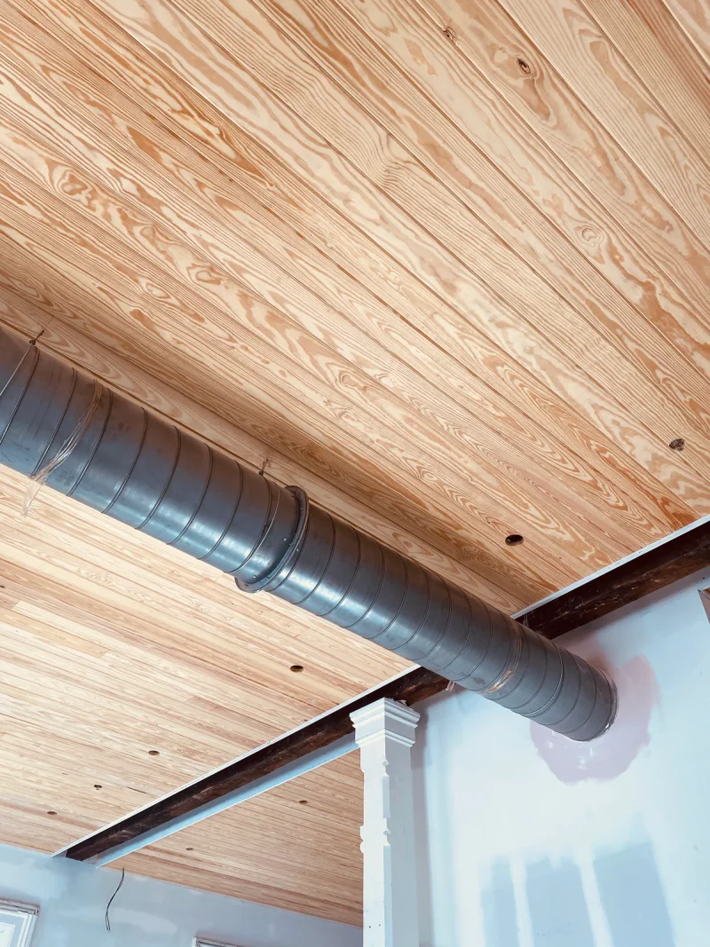 Pine plank ceiling fitted neatly around exposed spiral ductwork and a steel beam