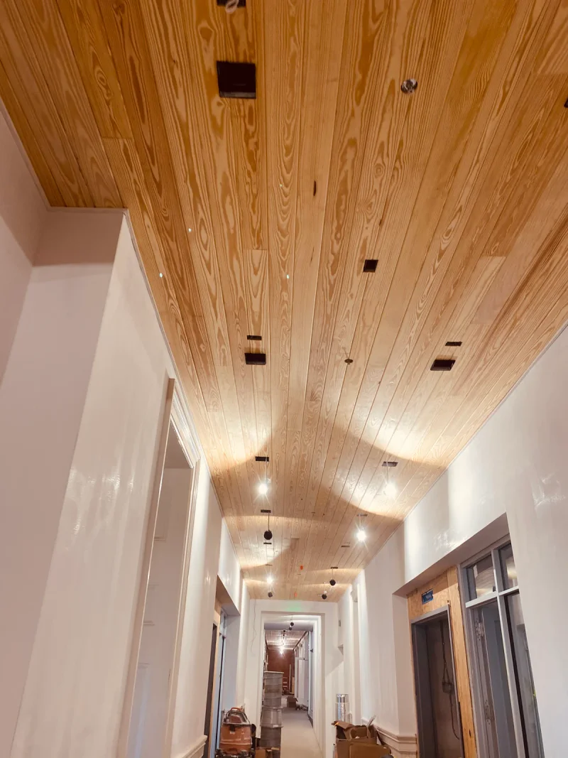 Corridor with a finished pine plank ceiling running above freshly painted white walls